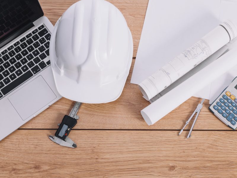 casco-y-planos-cerca-de-la-computadora-portatil